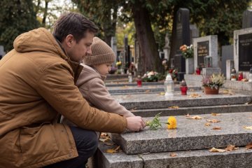 Rodič s dítětem pokládají květinu na hrob o Dušičkách